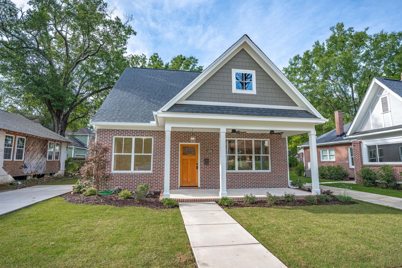 The finished house from the street — brick with a shingled gable and a deep front porch